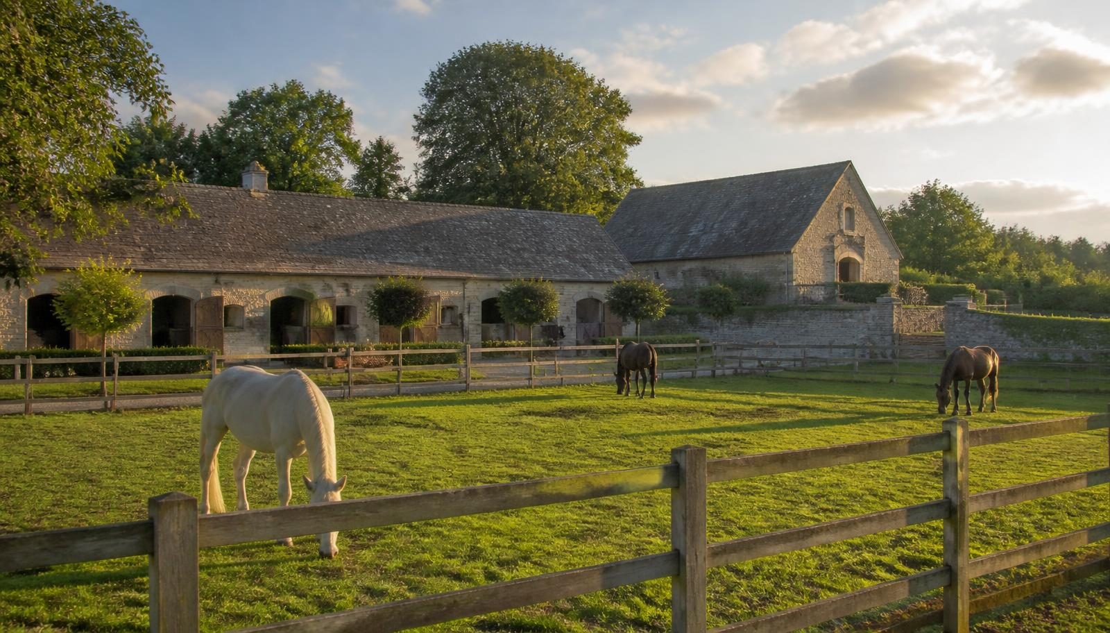 Horses grazing post-and-rail paddocks beside a traditional stone stable yard