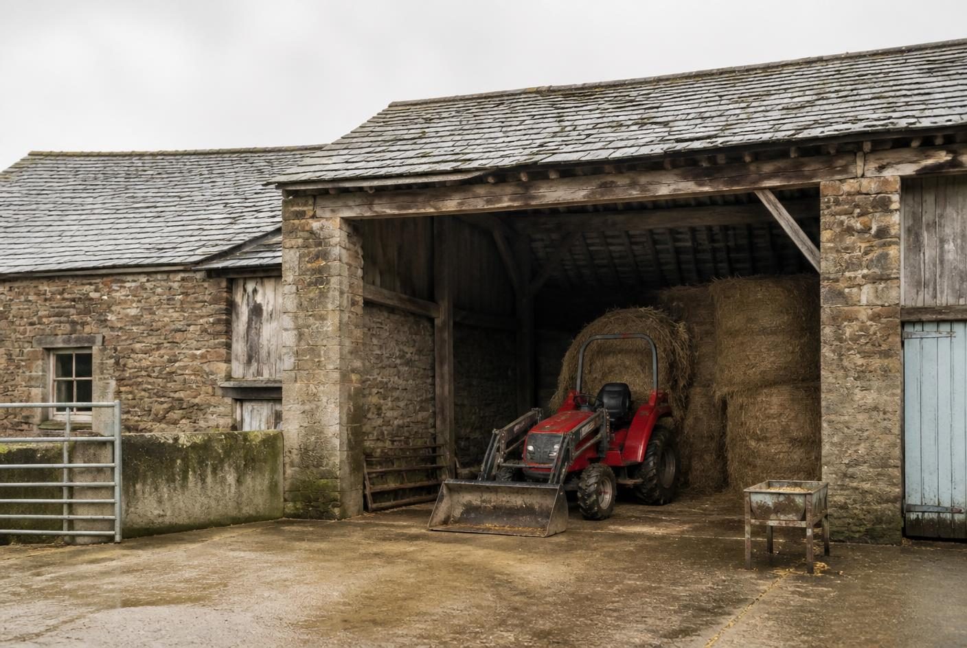 Stone smallholding barn with hay bales and a compact tractor in an open bay